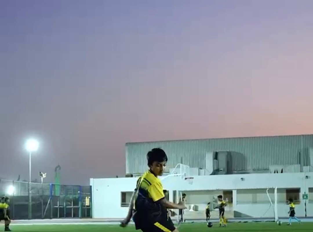 Child dribbling a football through cones at sunset